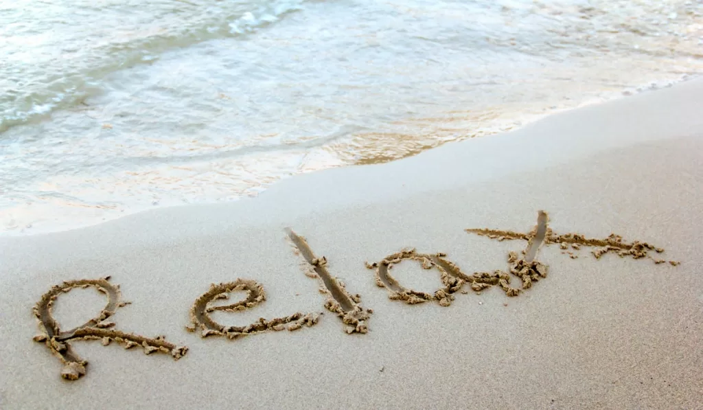the word relax written into the sand on a beach